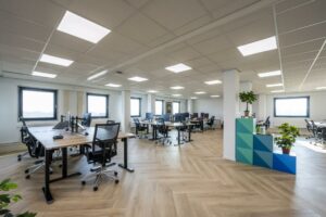 Moderne en lichte kantooruimte aan de Joan Muyskenweg met bureaus, bureaustoelen, computers en groene planten.
